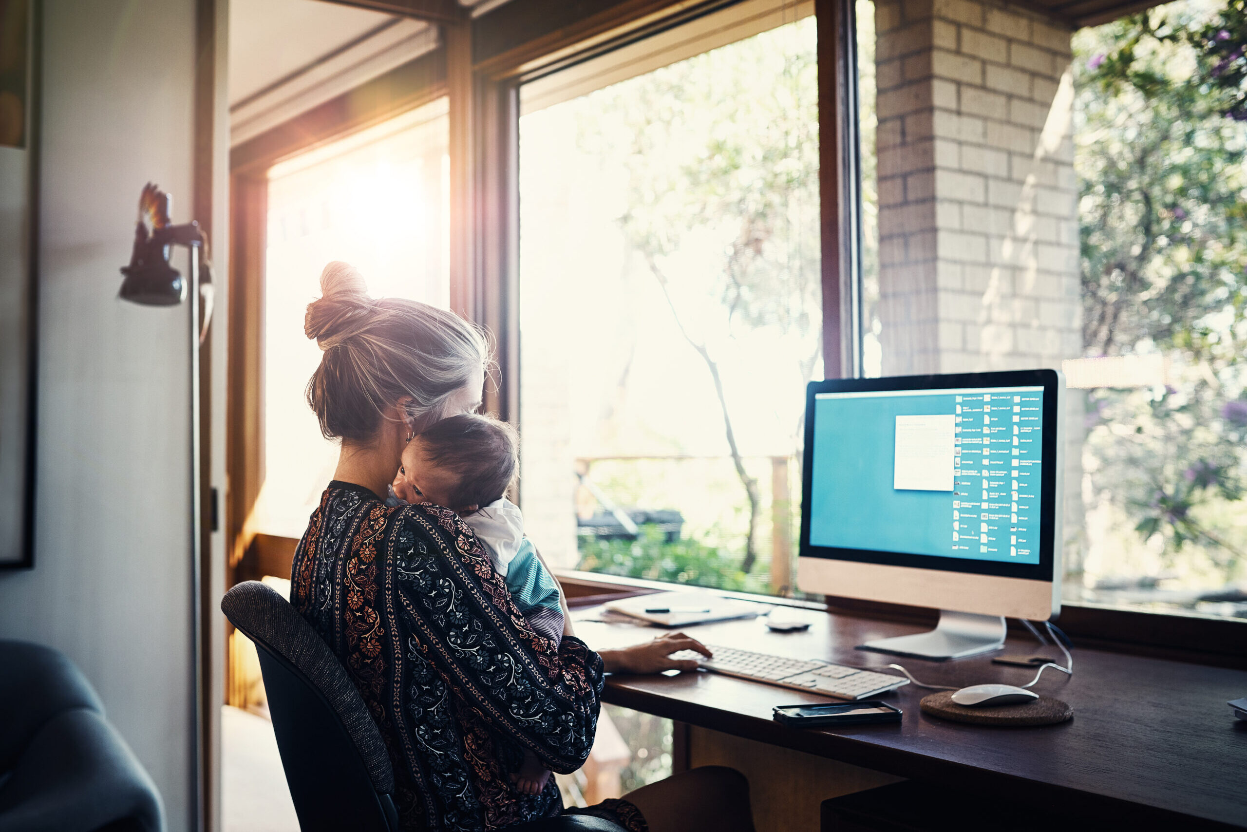 Shot of a young woman working at home while holding her newborn baby son